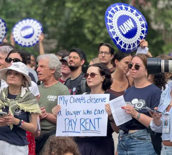 ALAA member at rally holding sign that says "my clients deserve a lawyer who can pay rent"